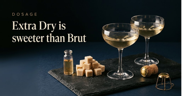 Two champagne coupes on a dark slate board, a dosage vial and a small mound of raw sugar cubes beside a used cork and wire cage — Extra Dry is sweeter than Brut