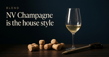 Several Champagne corks from different years laid beside a blending glass of pale straw wine and a wine thief on dark wood — NV Champagne is the house style
