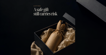A wine bottle wrapped in plain brown paper with twine sits in an open gift box beside crumpled tissue — A safe gift still carries risk