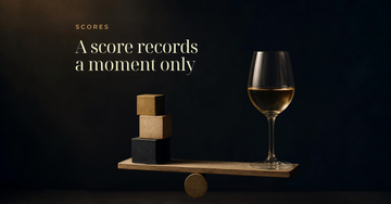 A wine glass sits on a small balance beam beside a stack of numbered wooden blocks on a dark surface — A score records a moment only