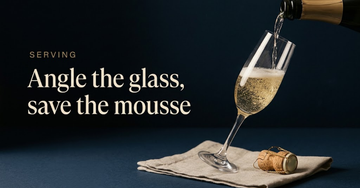 A champagne flute tilted to catch a slow pour, bubbles rising through pale gold liquid, a cork and wire cage on a linen napkin — Angle the glass, save the mousse