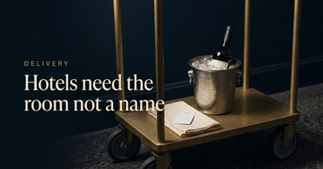A brass hotel corridor trolley holding a wine bottle in an ice bucket, a folded napkin and a blank key card — Hotels need the room not a name