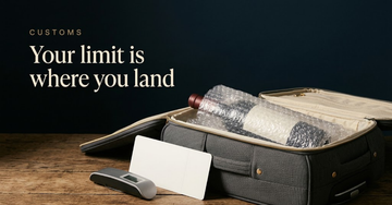 A wine bottle wrapped in bubble padding inside an open suitcase beside a blank boarding pass and a small luggage scale — Your limit is where you land