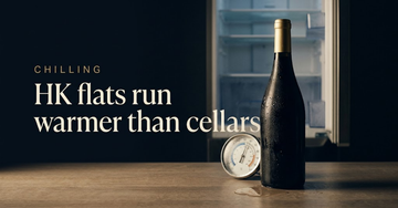 A wine bottle sweating beside a thermometer on a small flat kitchen counter, an open refrigerator door behind — Hong Kong flats run warmer than cellars