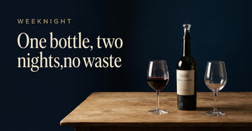 One opened wine bottle fitted with a vacuum stopper beside two glasses, one full and one empty, on a small kitchen table — One bottle, two nights, no waste