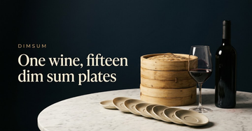A stack of bamboo steamers beside one wine glass and bottle, a row of empty small saucers fanned across a marble table — One wine, fifteen dim sum plates