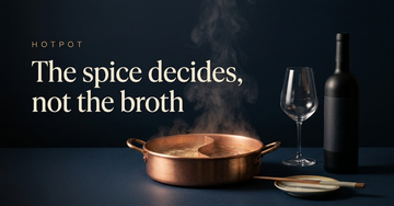 A copper hotpot ring with simmering broth beside a single wine glass and bottle, chopsticks resting on a small dish — The spice decides, not the broth