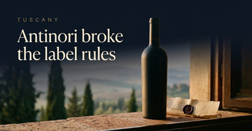 An unlabelled bottle on a terracotta sill beside a torn strip of parchment and a wax seal, cypress trees in hazy hills below — Antinori broke the label rules