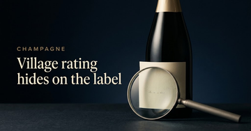 A magnifying glass resting over a blank cream label propped against an unlabelled Champagne bottle — Village rating hides on the label