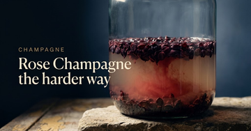 Dark red grape skins steeping in pale juice inside a glass vat, rose tint spreading slowly under cool cellar light — Rose Champagne the harder way