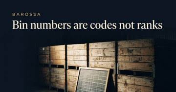 Stacked wooden storage crates with faded stencil marks in a dim warehouse aisle, a chalkboard tally leaning against the base — Bin numbers are codes not ranks