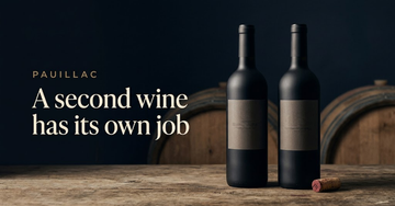 Two similar dark bottles of red wine side by side on a cellar table, one cork freshly pulled, oak barrel shadows behind — A second wine has its own job