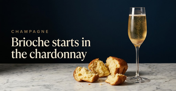 Torn pieces of fresh brioche beside a flute of golden Champagne on a marble counter, lees visible through the base of the glass — Brioche starts in the chardonnay